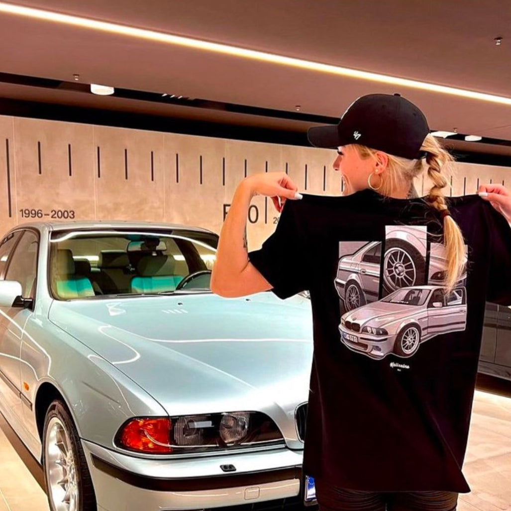 A person showcasing a custom illustration T-Shirt with a car image on it, in front of a BMW car.